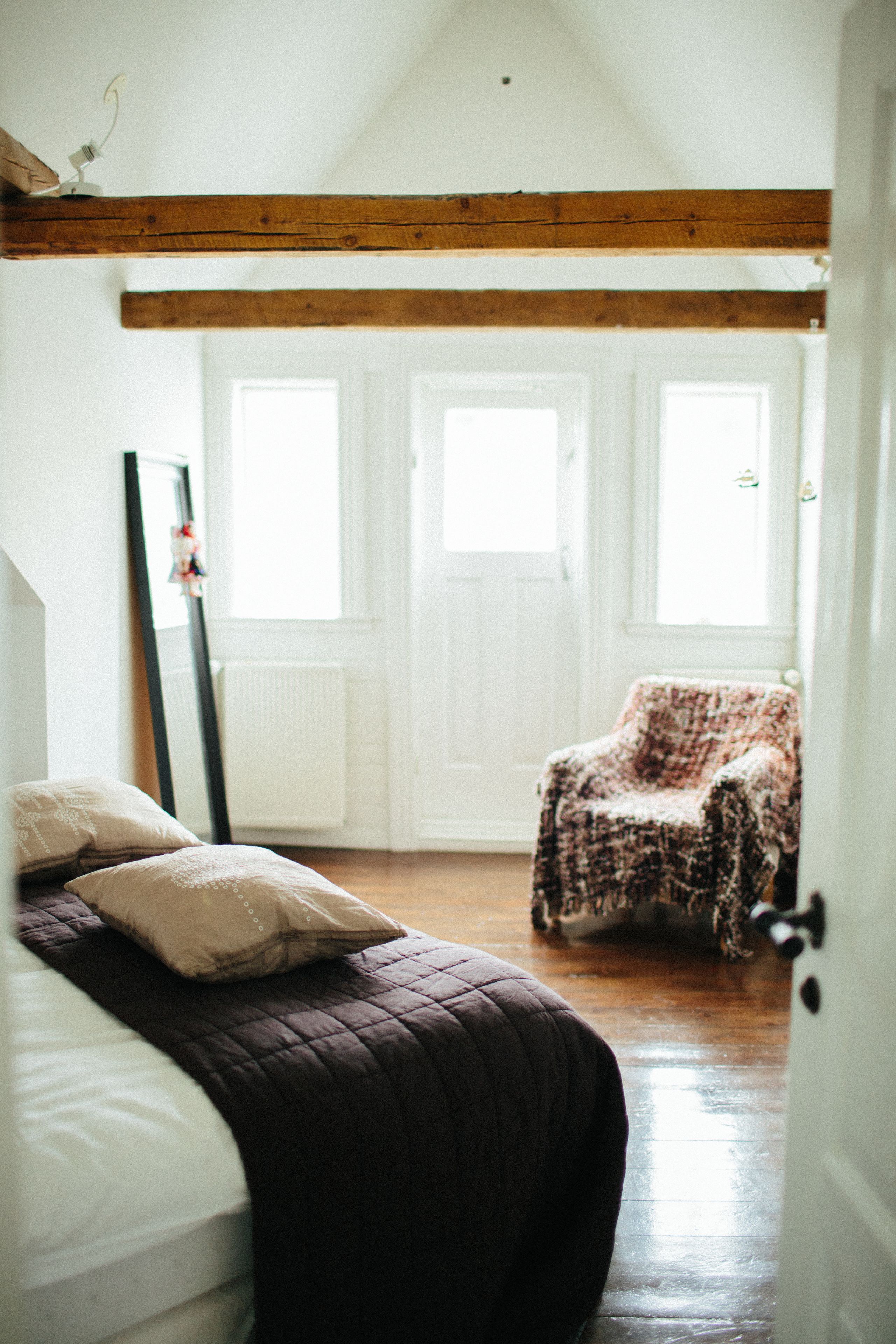 Un dormitorio con cama, una silla y una puerta que da a otra habitación.