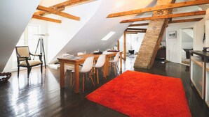 A dining area with a wooden table and chairs, a red rug, and exposed wooden beams. - Hoepfner  Historical House (Akureyri)