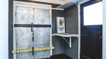 A room with a large metal door, a small shelf with a sign, and a window.