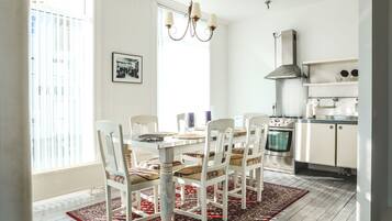 Un comedor con una mesa y sillas blancas, una araña y una cocina al fondo.