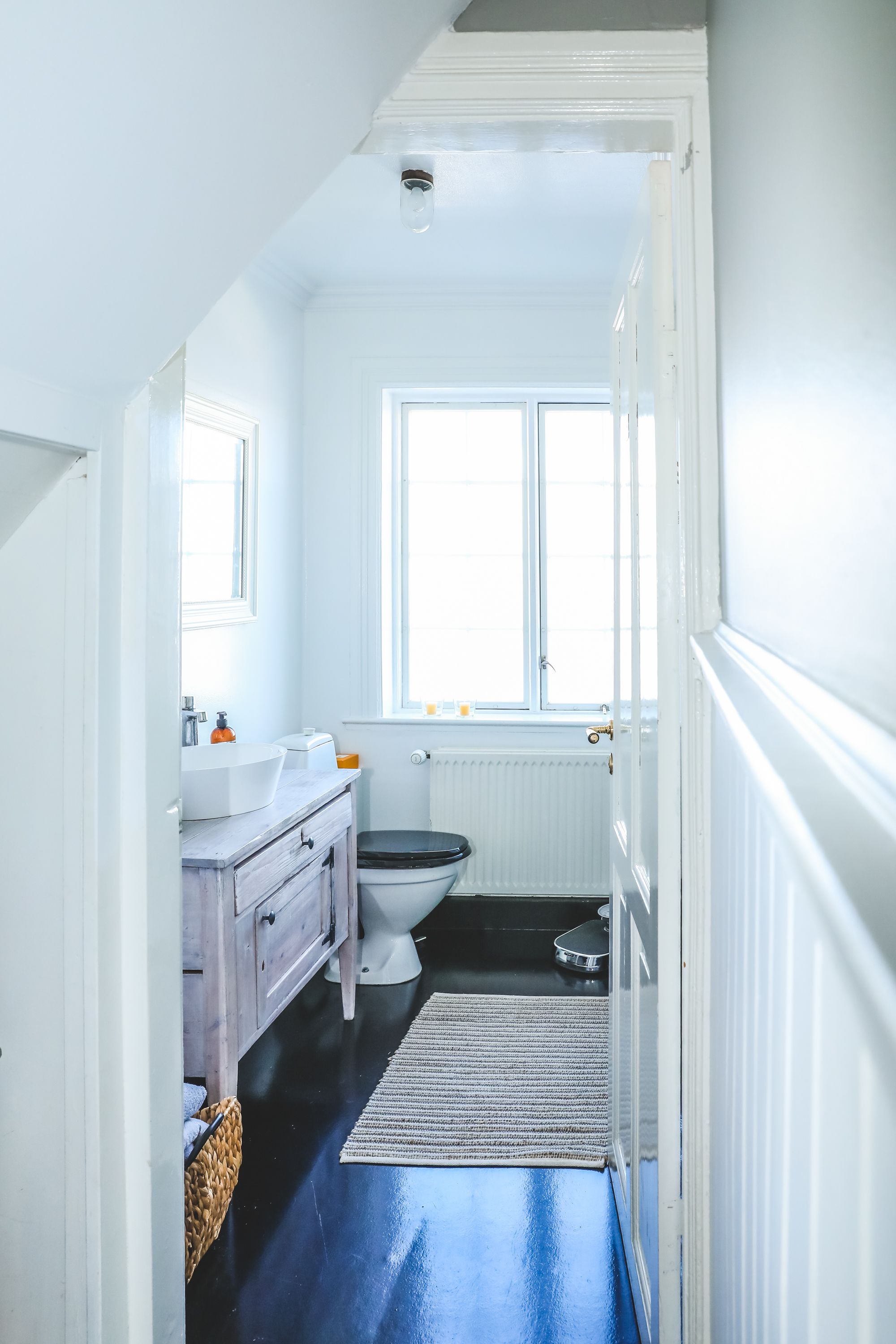 A narrow bathroom with a white sink, a toilet, and a window.