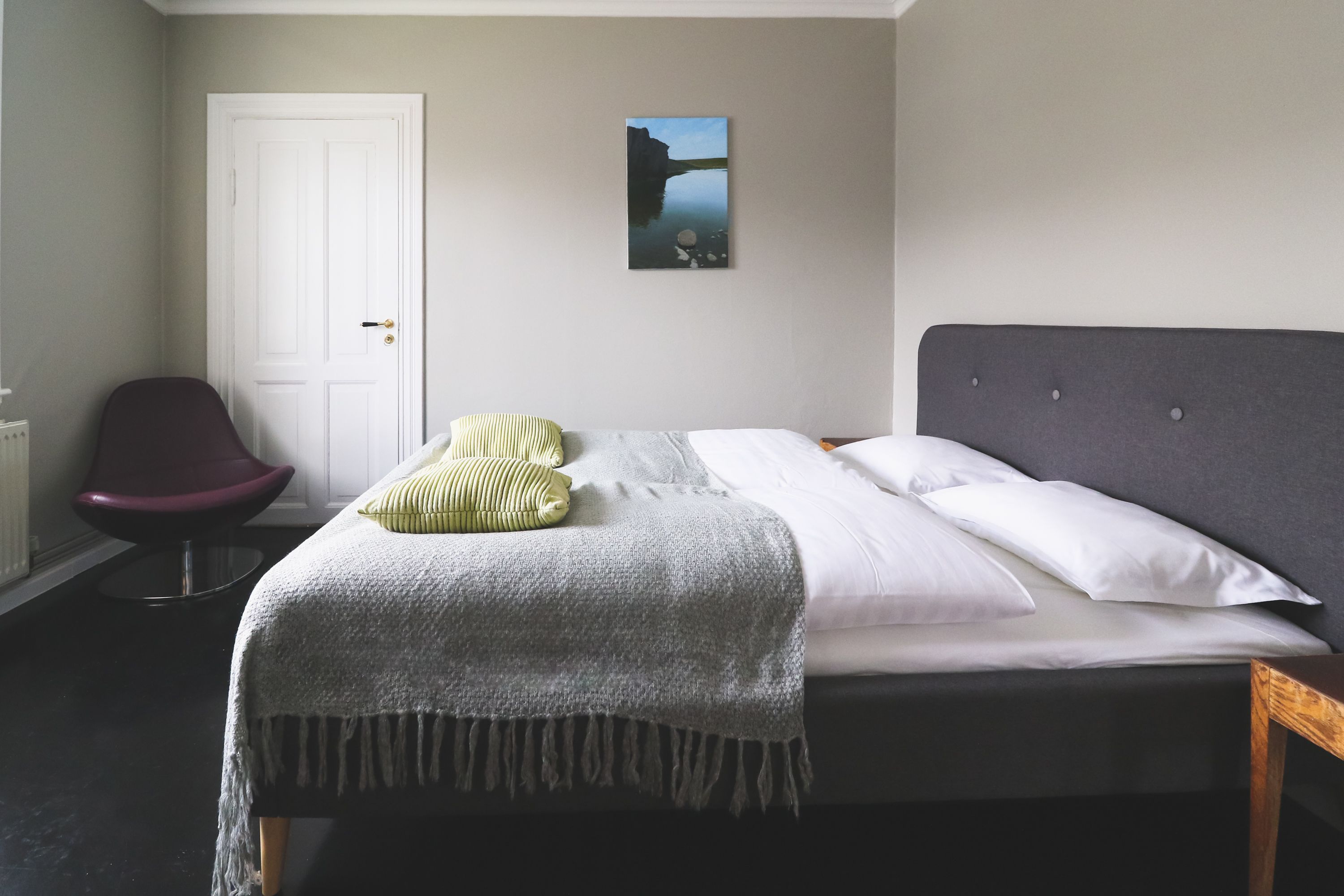 A bedroom with a bed, a chair, a door, and a wall-mounted picture.