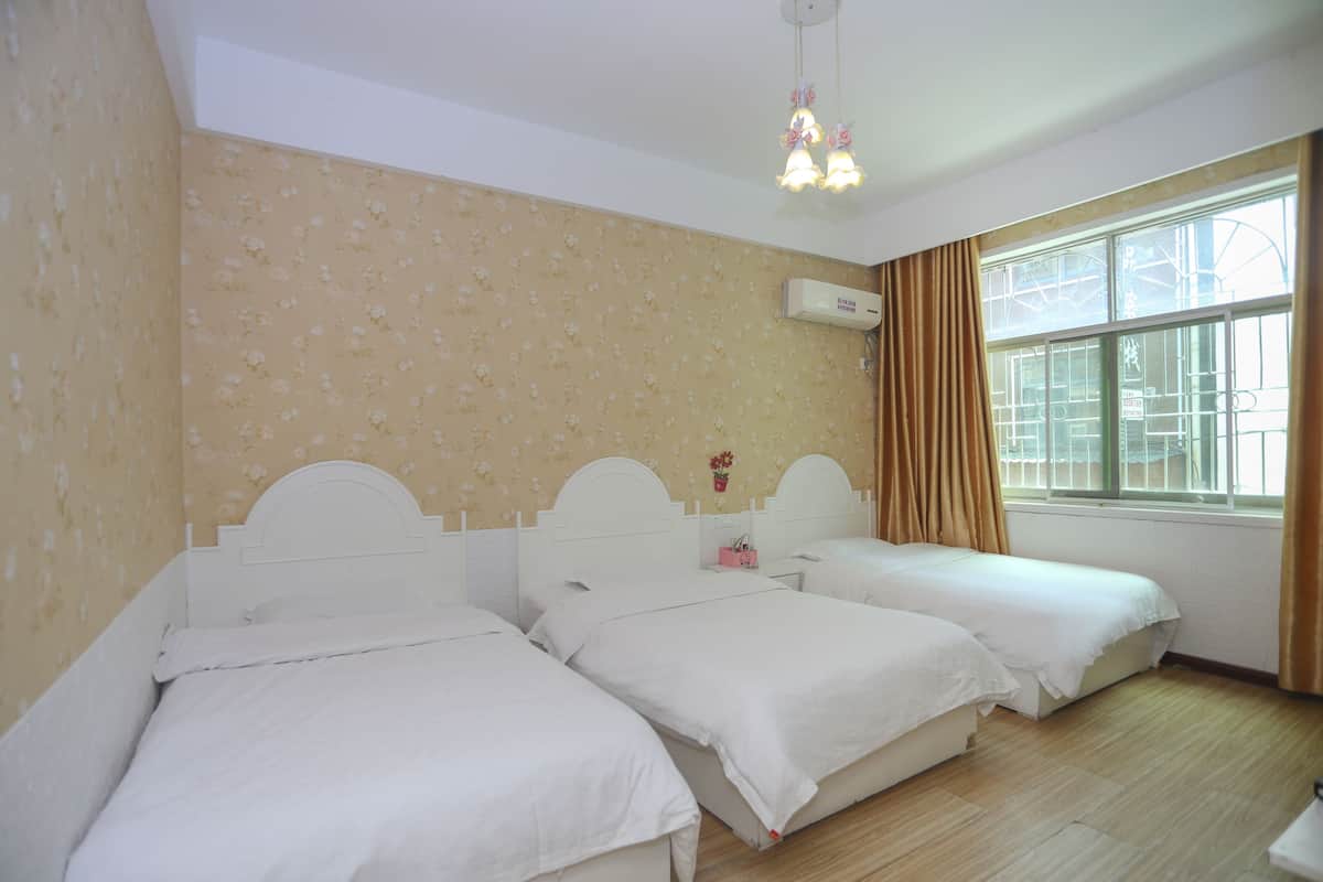 A room with two single beds, a window with curtains, and an air conditioning unit on the wall.