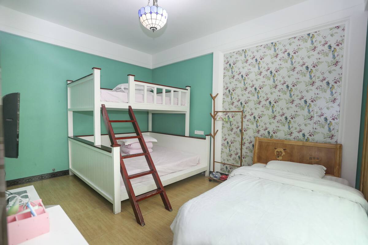 A bunk bed room with a ladder, a wooden headboard, and a floral wallpaper.