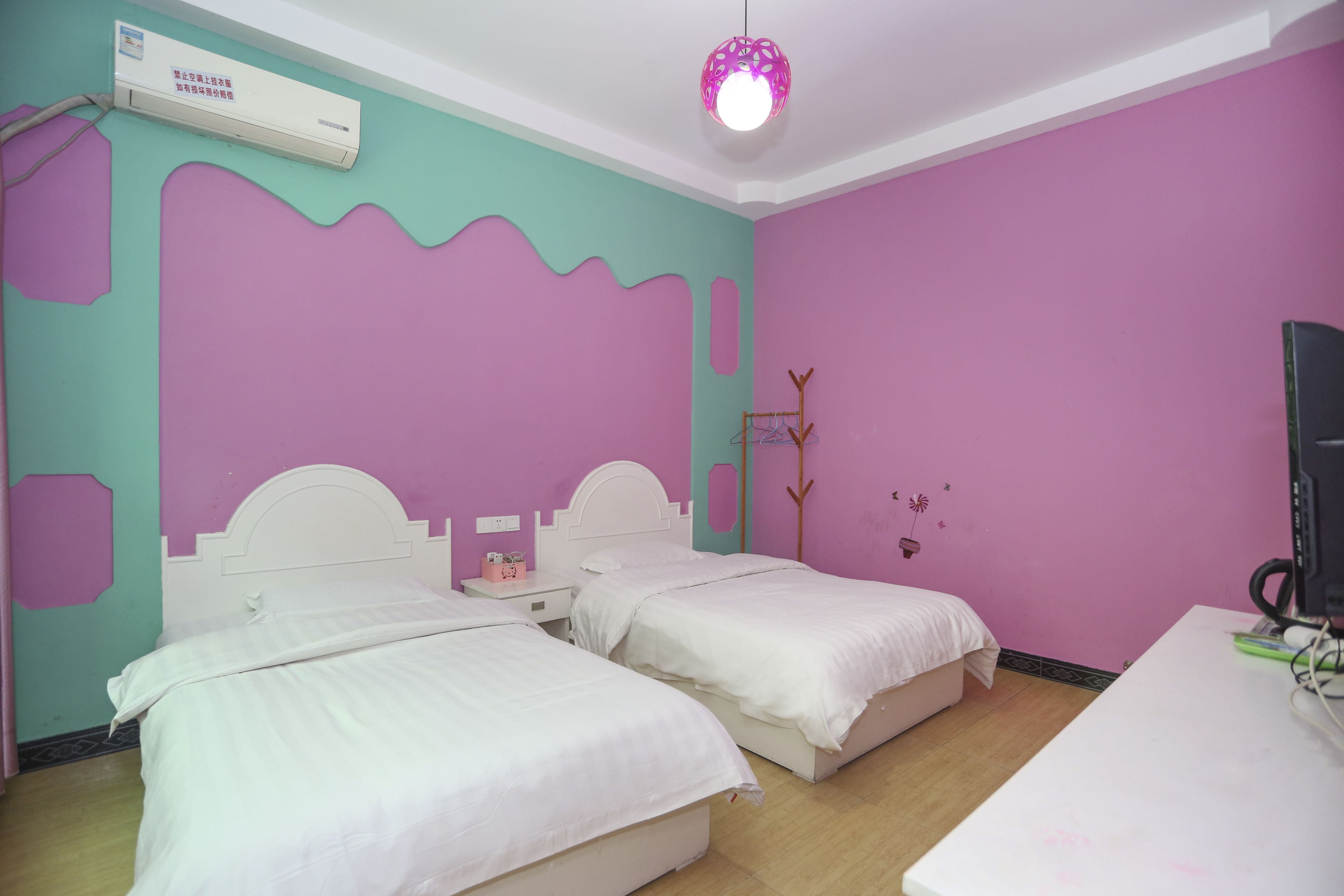 A room with two beds, a desk, and an air conditioning unit.