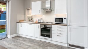 Uma cozinha moderna com armários brancos, forno Bosch, micro-ondas e coifa de vidro.