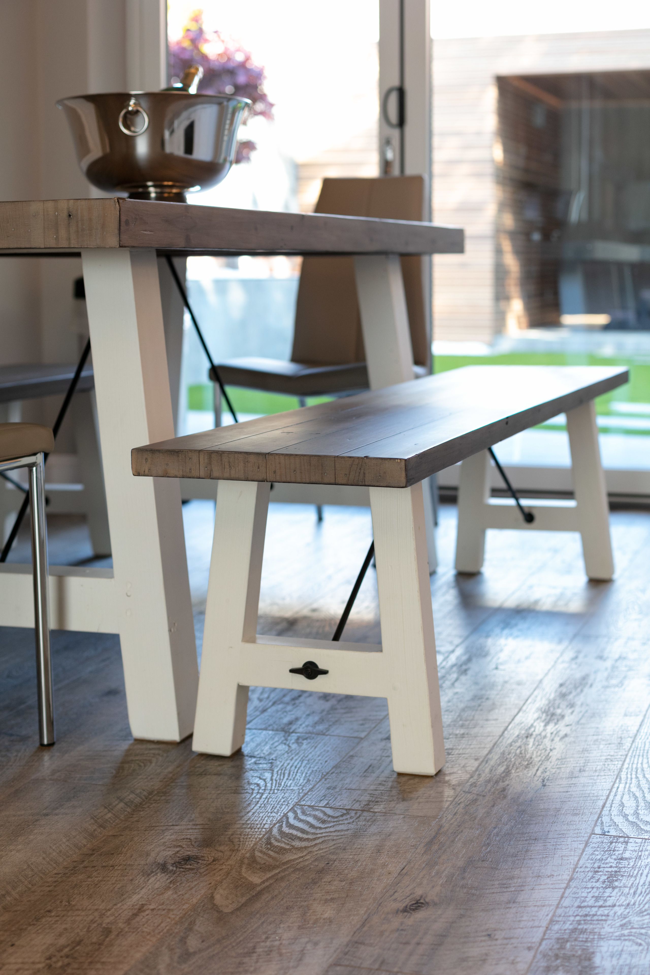 A wooden bench with a metal bowl on top, placed on a white table with metal legs.