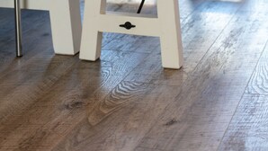 Um banco de madeira com uma tigela de metal em cima, colocado sobre uma mesa branca com pés de metal.