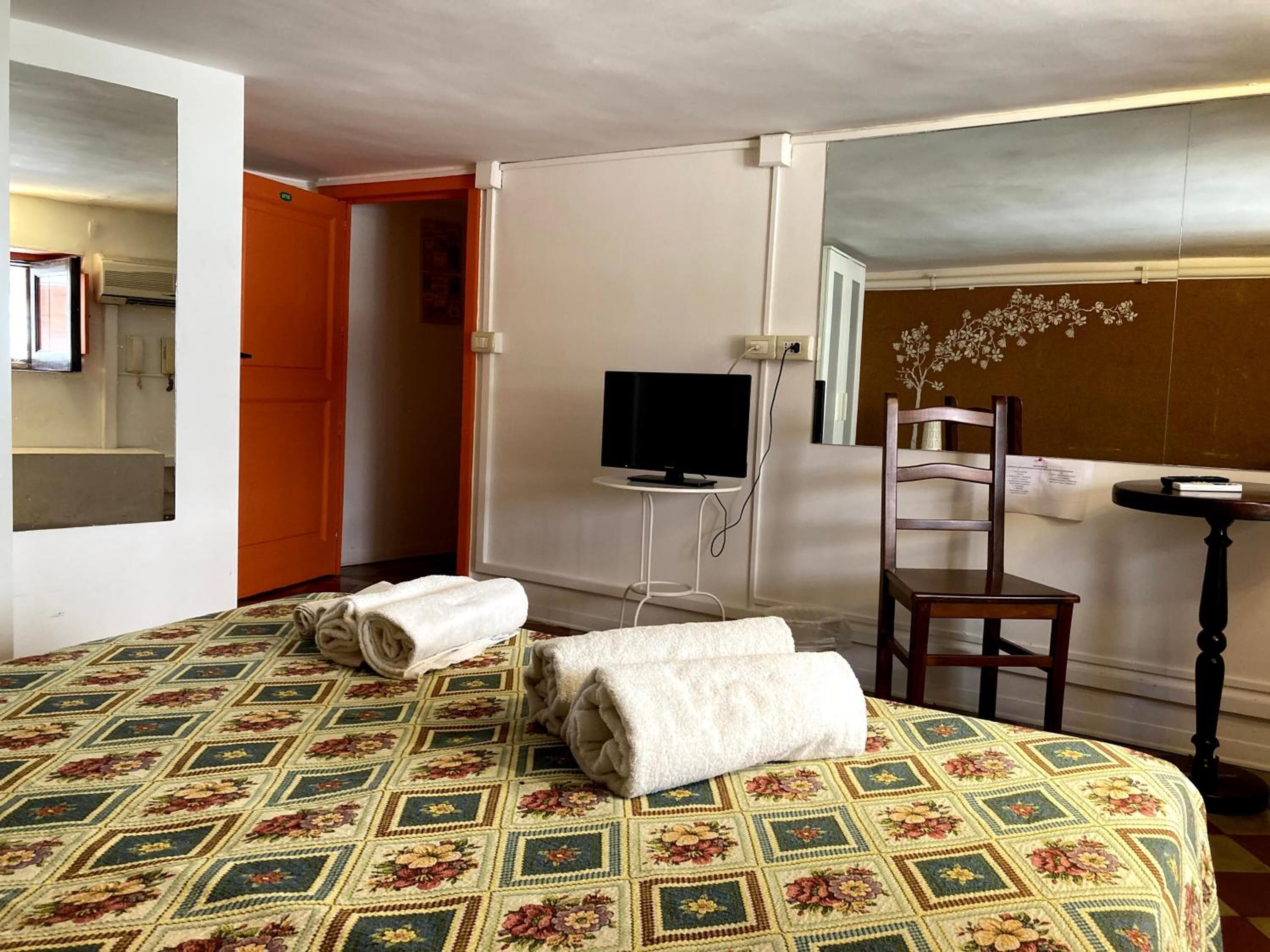Una habitación de hotel con cama, televisión, una silla y una mesita.