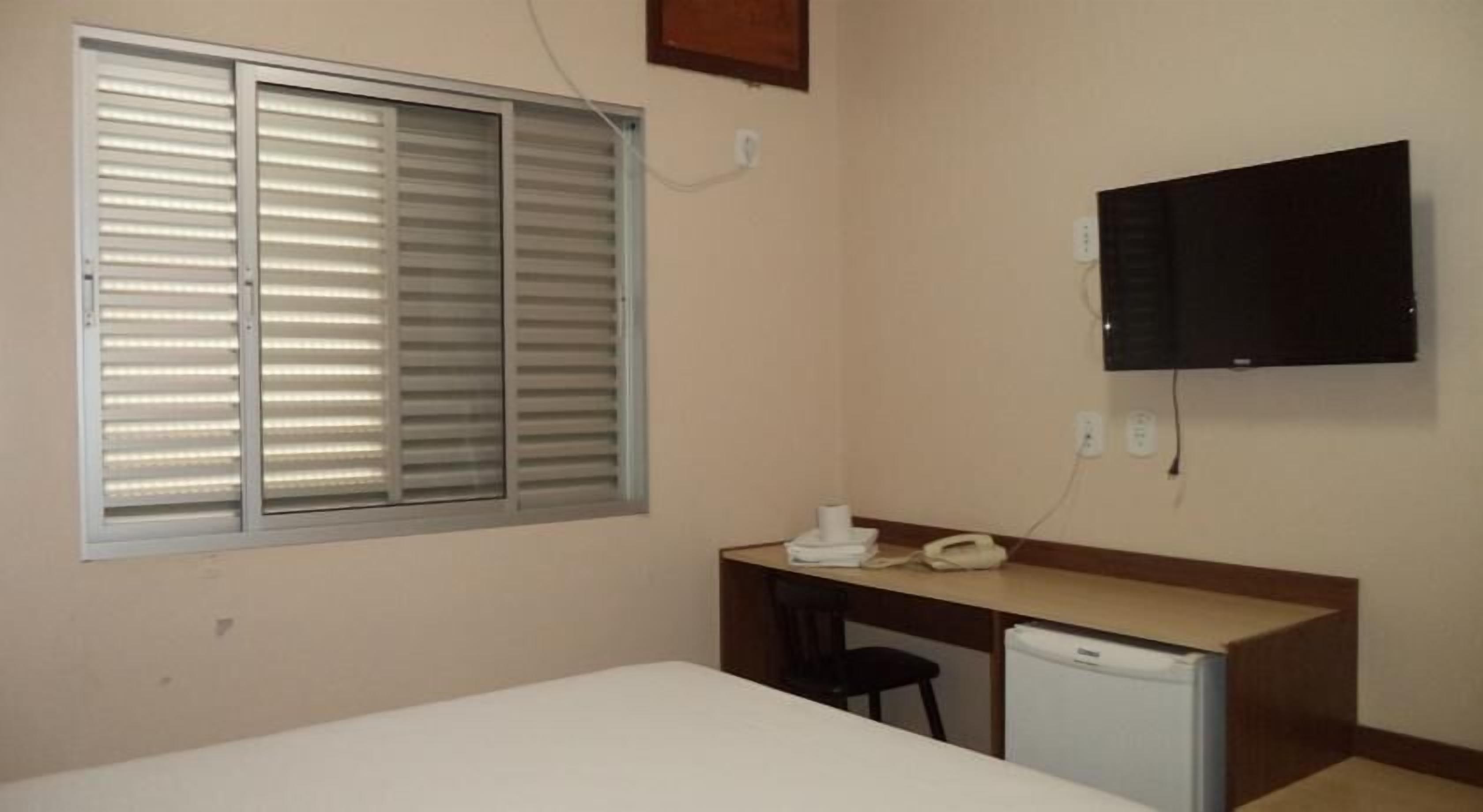 A small room with a bed, a desk, a chair, a television, and a refrigerator.
