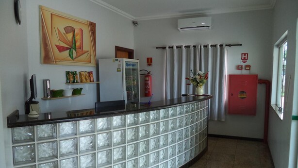A reception area with a glass partition, a refrigerator, a fire extinguisher, and a wall-mounted air conditioning unit. - Villa Verde Hotel (Navirai)