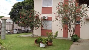 A two-story building with a red-tiled roof, multiple windows with shutters, and a small garden area with potted plants and a lawn. - Villa Verde Hotel (Navirai)