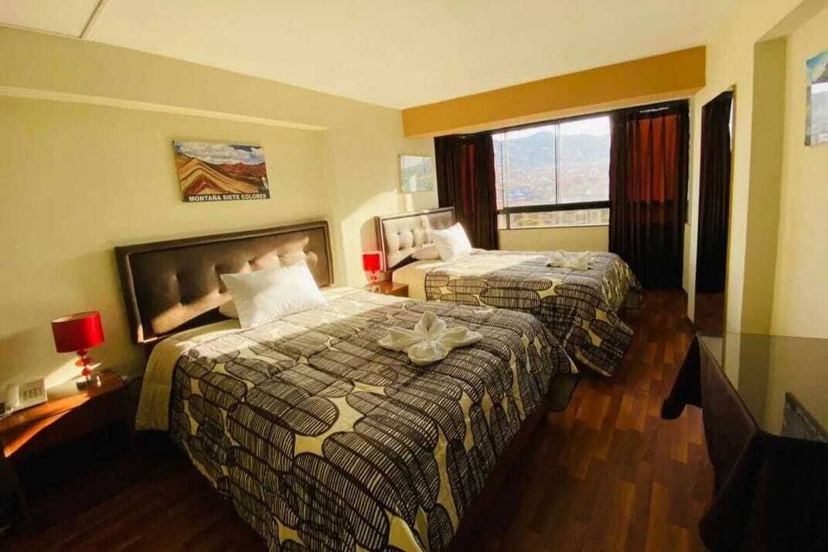 A hotel room with two beds, a wooden floor, a painting on the wall, and a window with curtains.