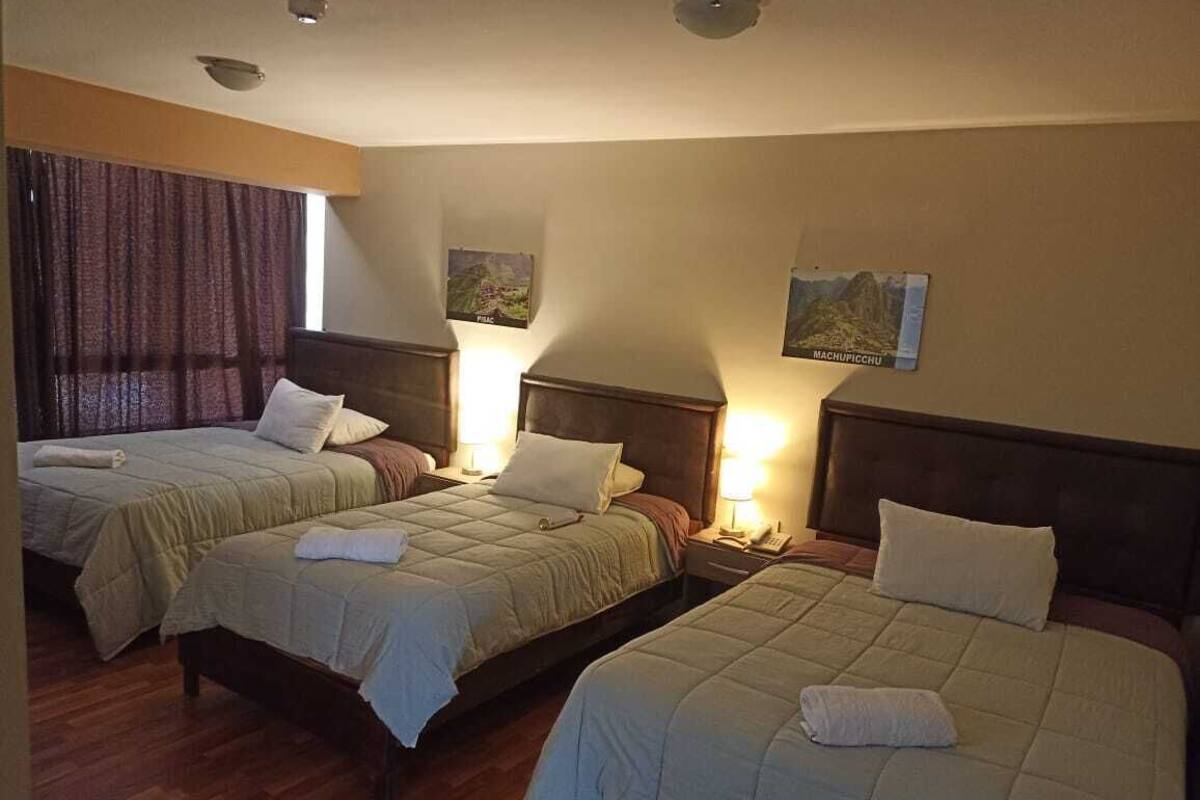 A hotel room with three beds arranged in a row, each with a headboard and bedside tables.