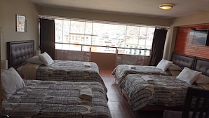 Habitación de hotel con dos camas, un ventanal grande con vista a la ciudad y cabecero de madera a la derecha.
