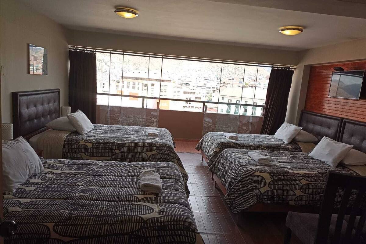 A hotel room with two beds, a large window with a city view, and a wooden headboard on the right.