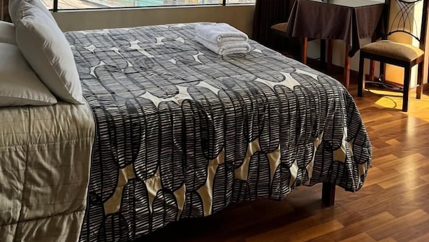 Una habitación de hotel con una cama grande, un televisor montado en la pared, una mesita y una silla.