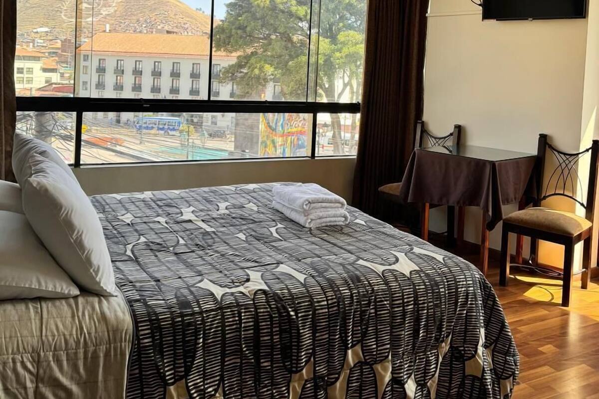 A hotel room with a large bed, a TV mounted on the wall, a small table, and a chair.