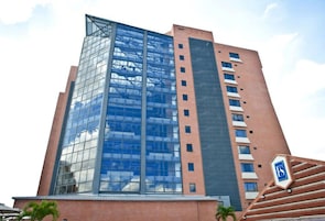 Edifício moderno com fachada de vidro e base de tijolos, apresentando um logotipo em destaque na lateral.