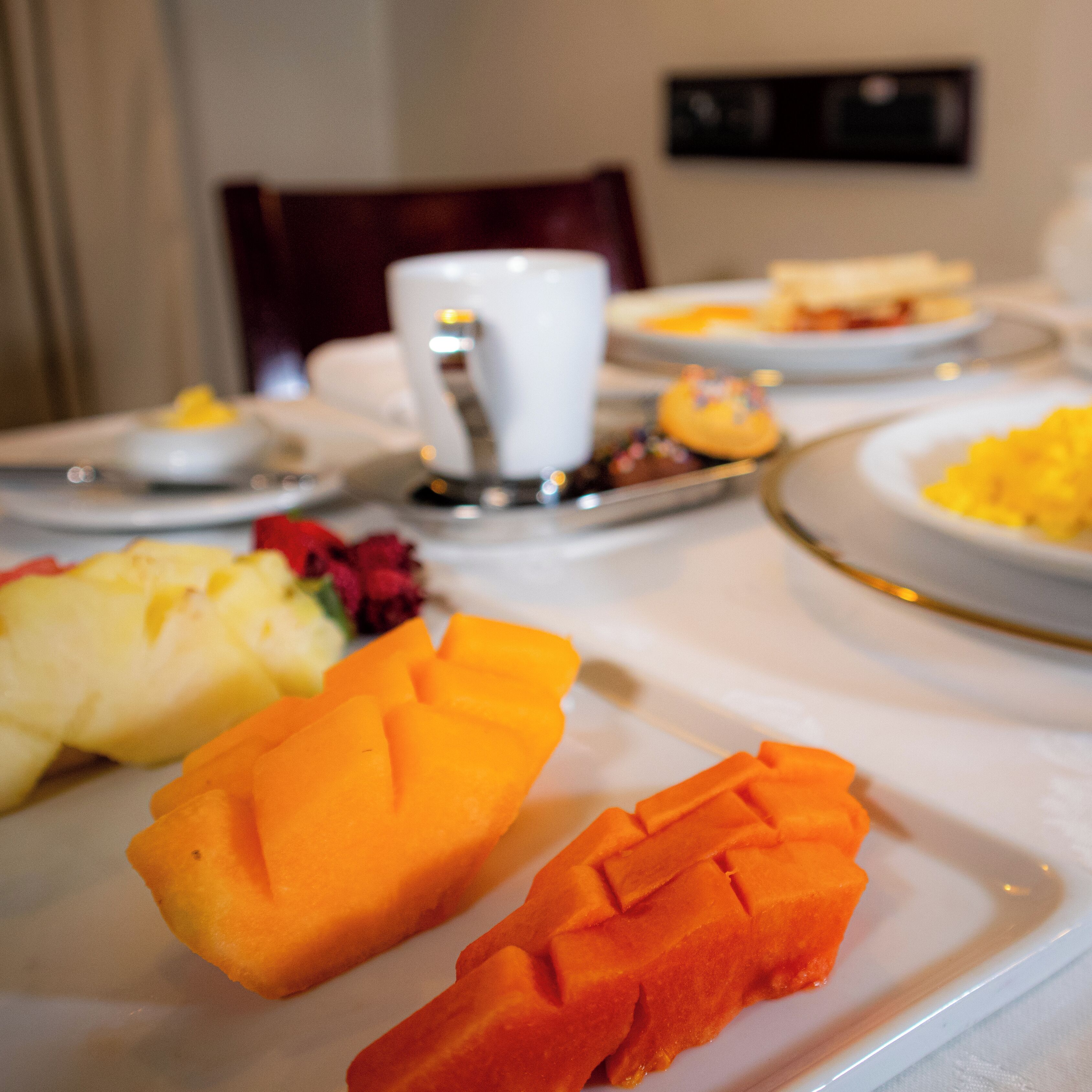 A dining table with plates of fruit and a white cup.