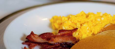 A plate with scrambled eggs, bacon, and pancakes.