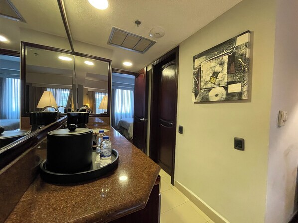 A hotel room with a marble countertop, a coffee machine, a mirror, a bed with curtains, and a wall-mounted artwork. - Executive Suites Valencia (Valencia)