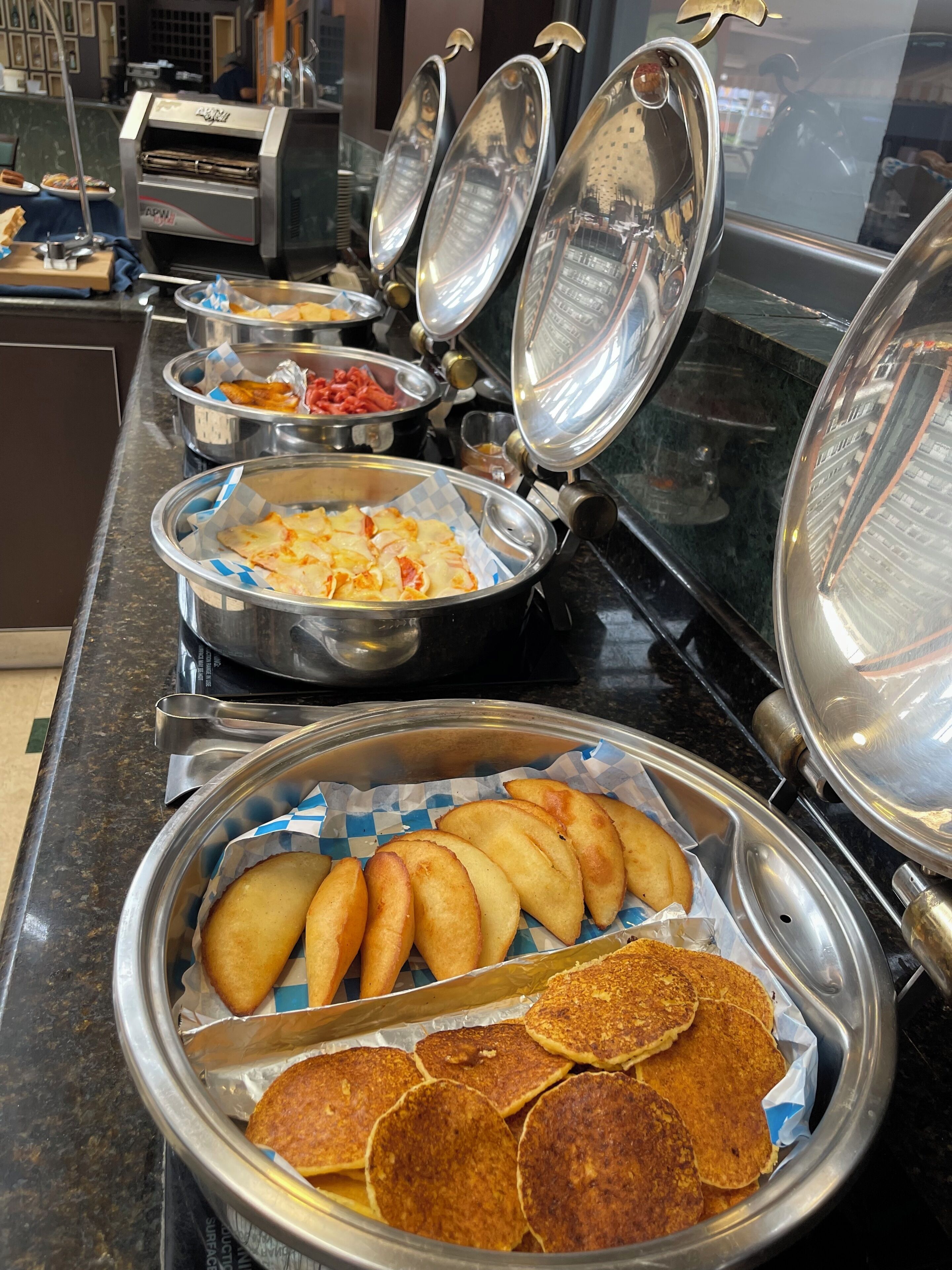 A buffet with various food items in metal containers, including what appears to be a selection of baked goods and possibly some meat dishes.