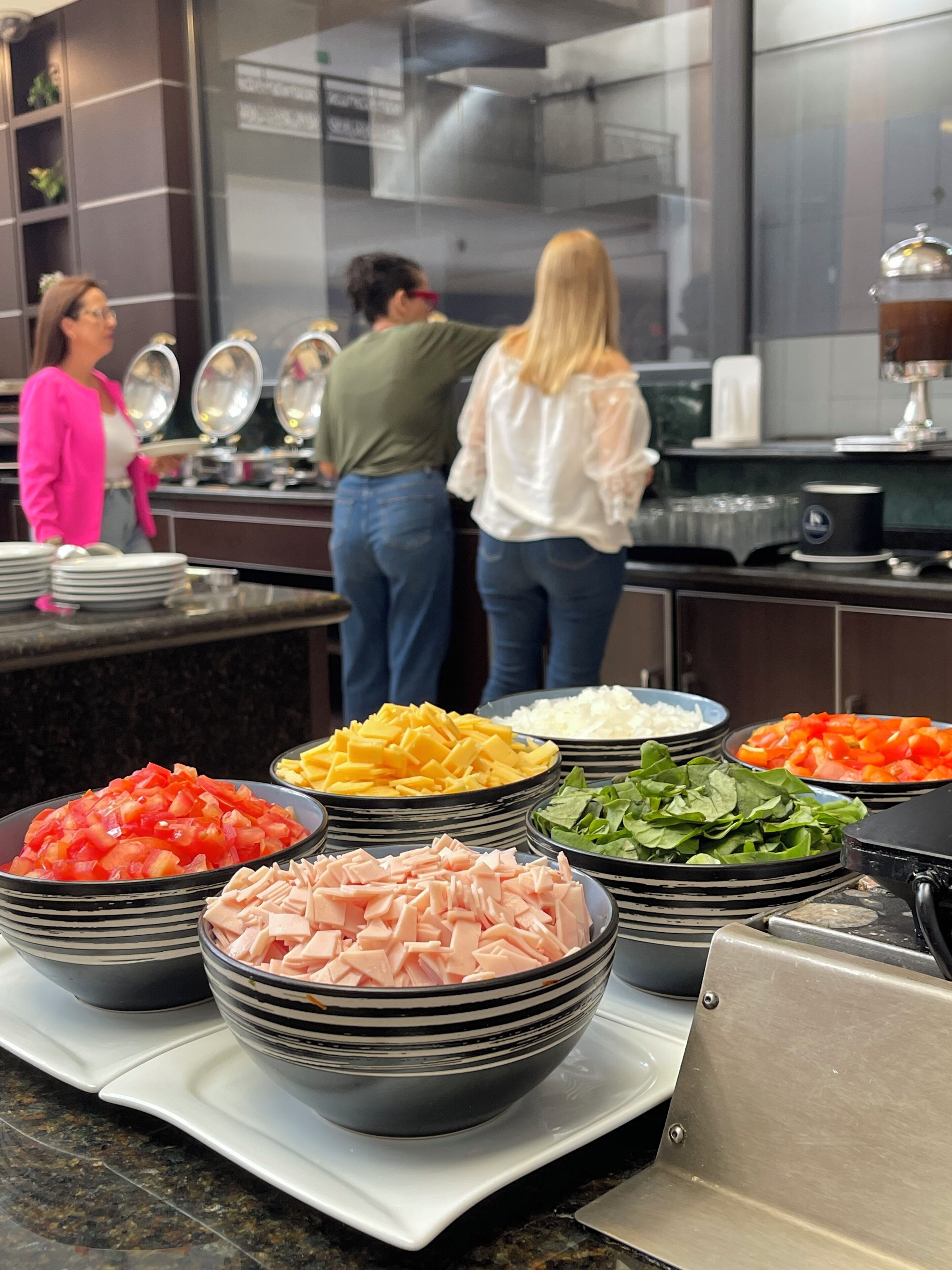 A buffet setup with various food items in bowls, a kitchen area with appliances, and a group of people standing by the counter.