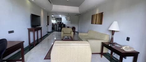 Una habitación de hotel con televisión, sofá, sillón, mesa de centro, lámpara y teléfono.