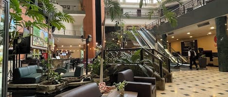 A spacious lobby with multiple seating areas, a central staircase, and a large atrium with natural light.