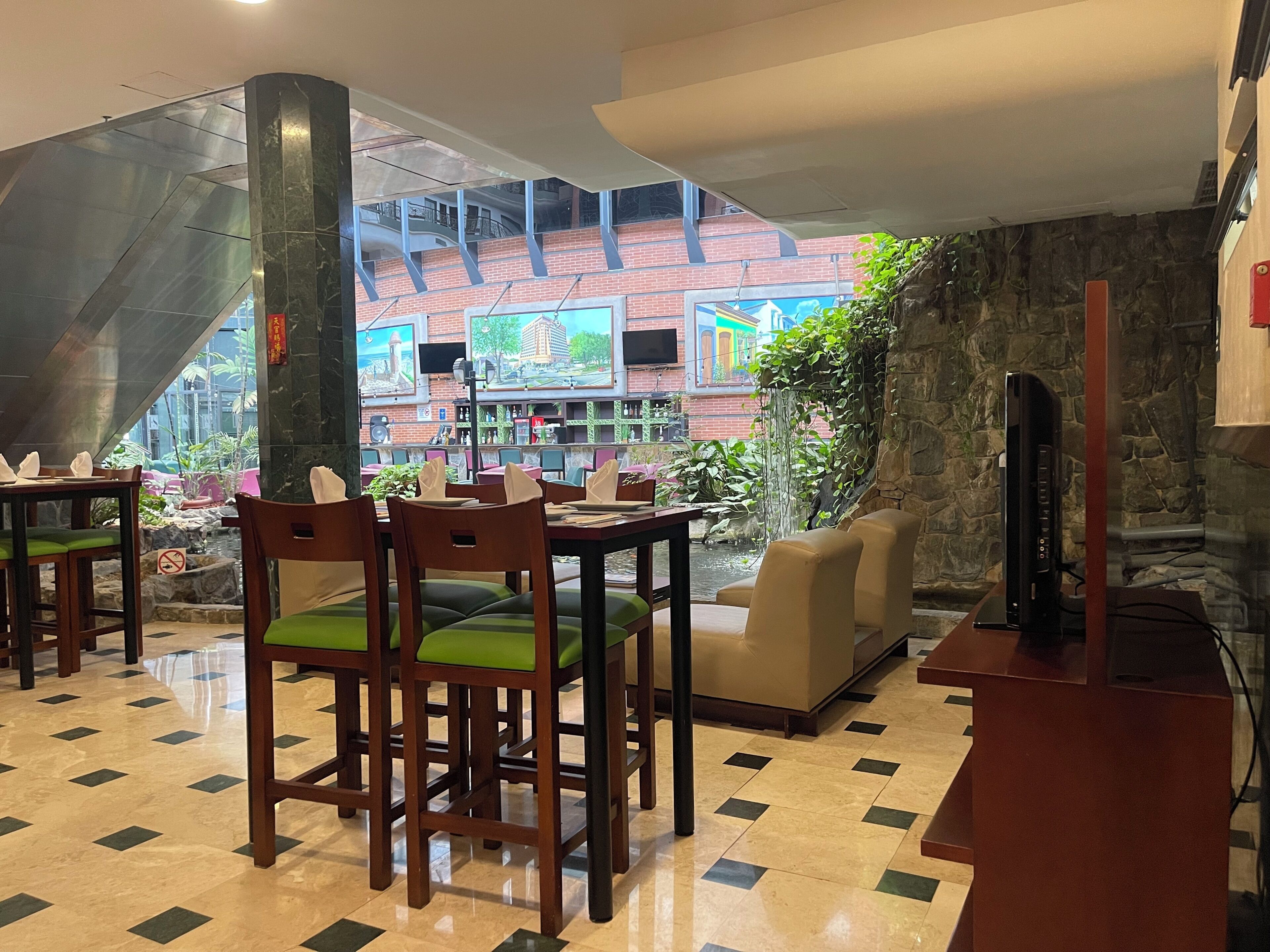 A restaurant with a view of a brick building and a waterfall. Tables and chairs are arranged for dining.