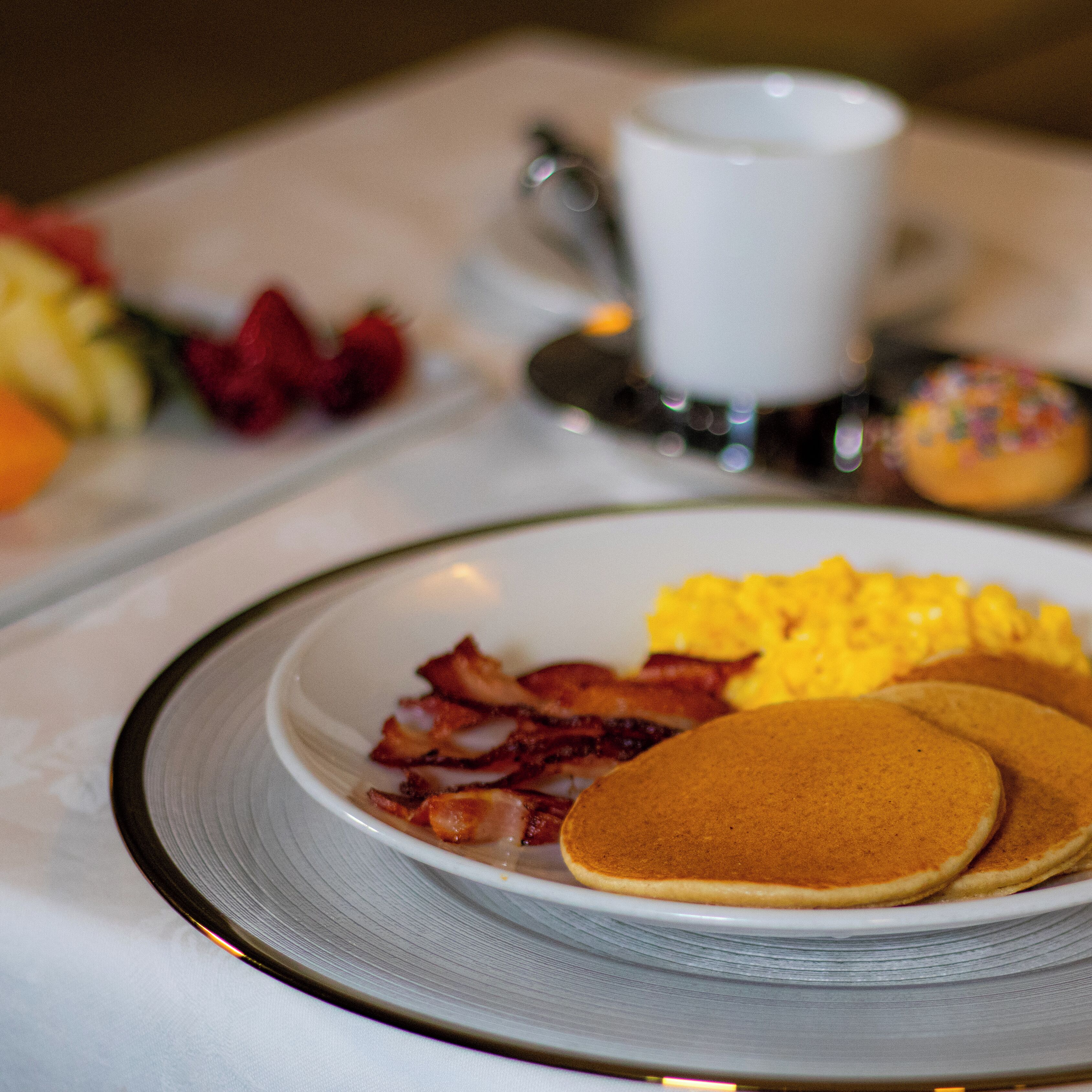 A breakfast plate with pancakes, bacon, and scrambled eggs.