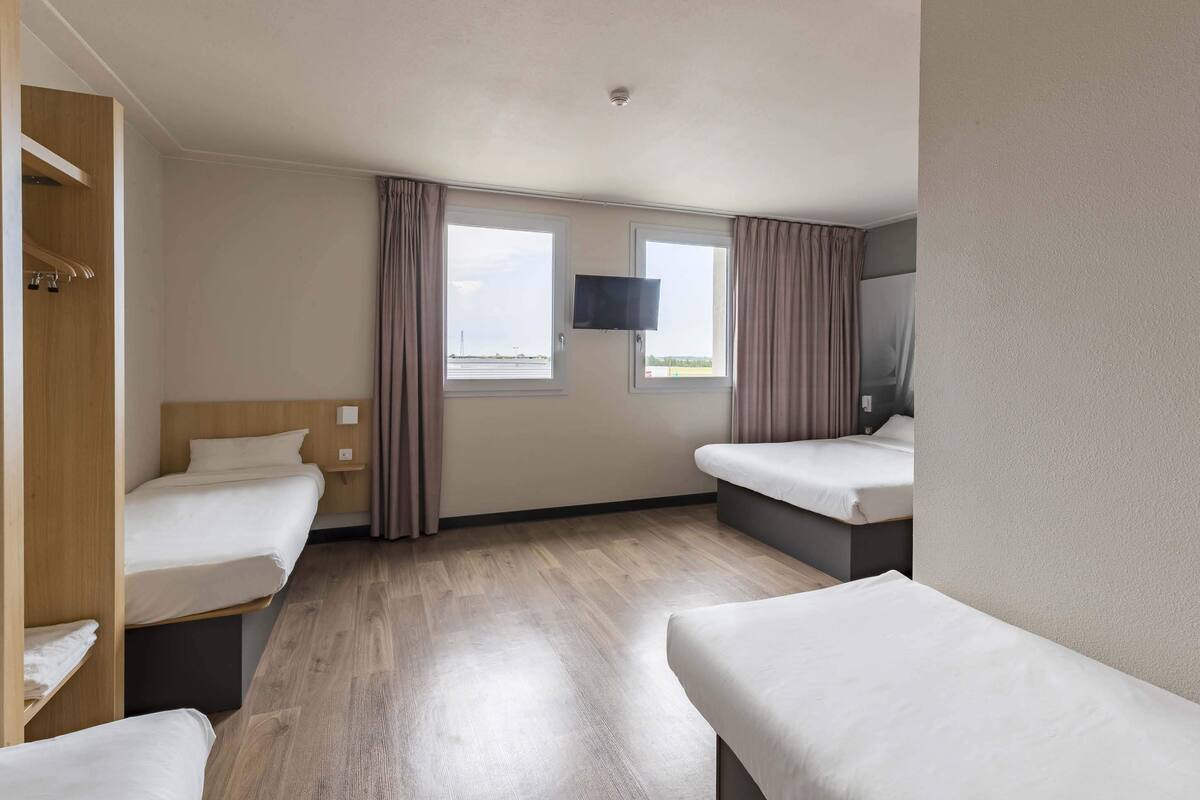 A hotel room with two beds, a TV, and a window with curtains.