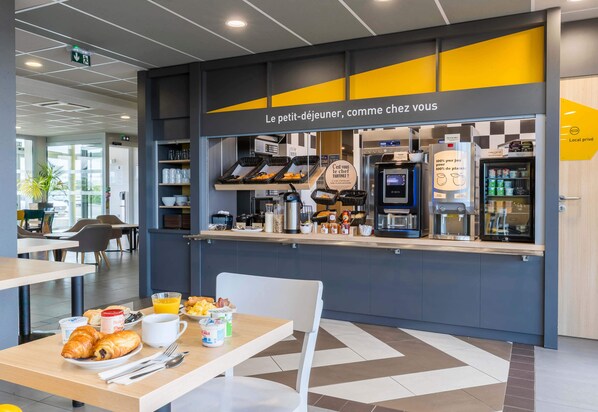 A breakfast area with a counter displaying pastries, a coffee machine, and a refrigerator.