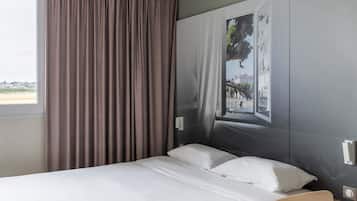 Une chambre d’hôtel avec un lit, une fenêtre avec des rideaux et une œuvre d’art accrochée au mur.