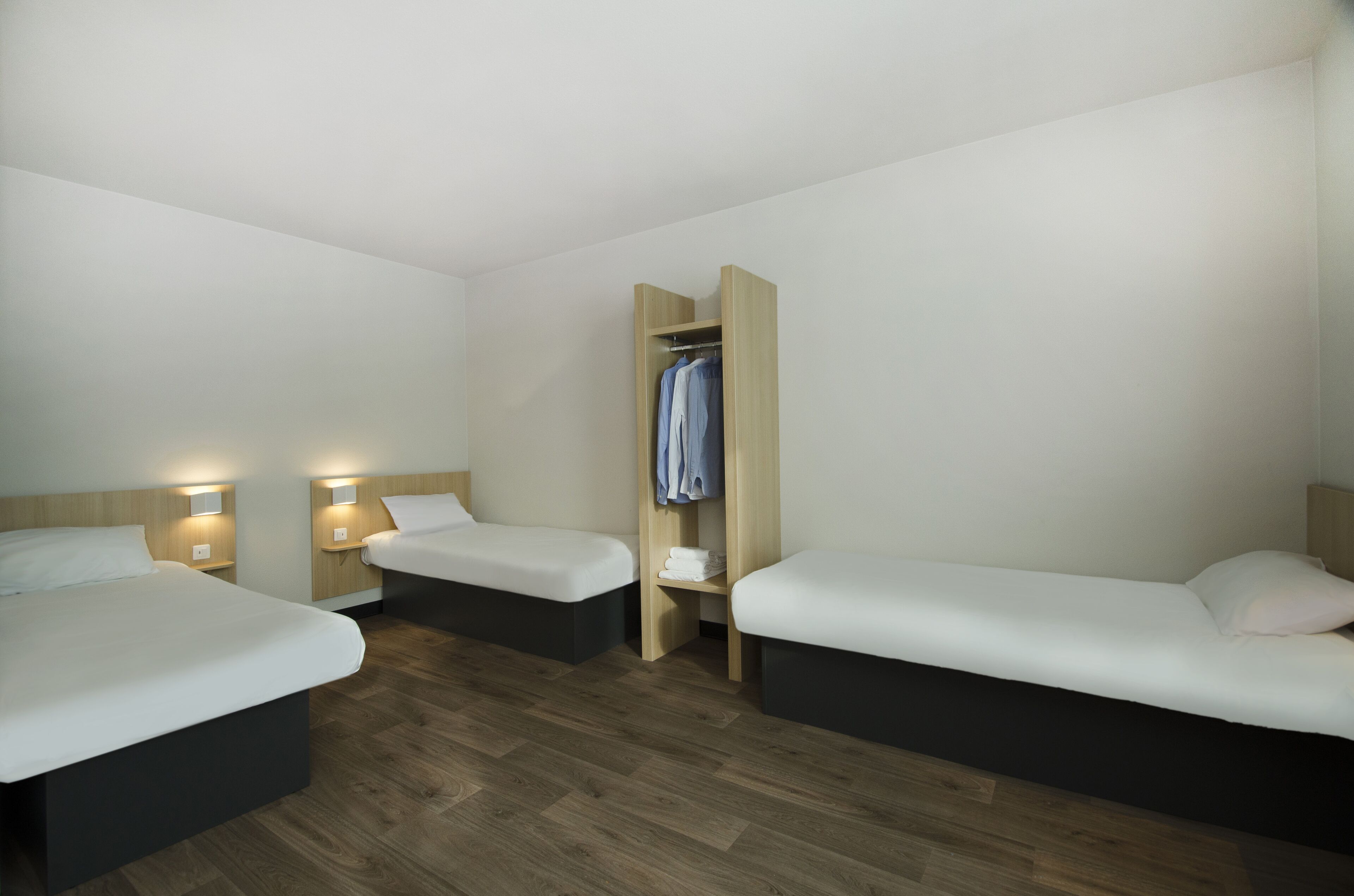 Camera d'albergo con due letti, un armadio e lampade da comodino.