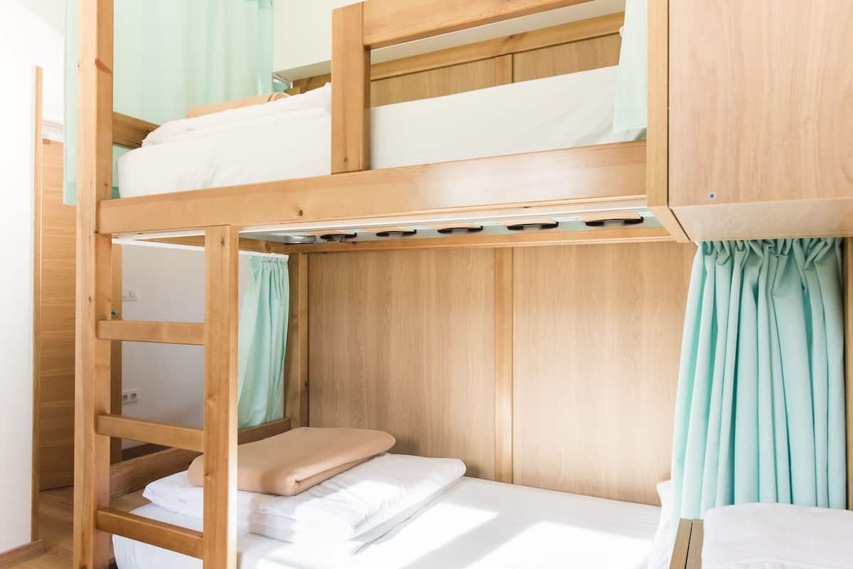 A bunk bed room with wooden frames, a ladder, and a curtain.
