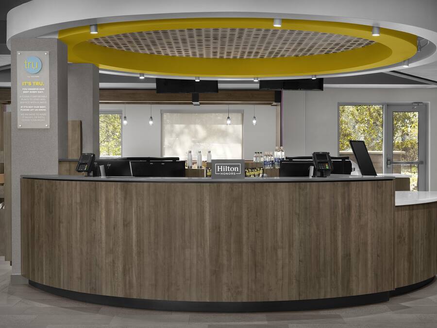 A modern hotel reception desk with a circular design, a digital information board, and a view of the outdoors through large windows.