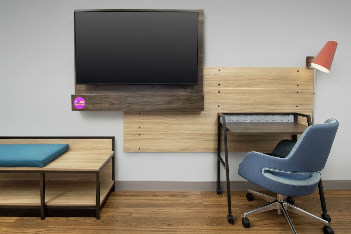 Una habitación moderna con una televisión de pantalla plana montada en una pared de madera, un escritorio con una silla y un banco con cojín.