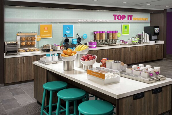 Una estación de desayuno con máquinas para hacer gofres, fuentes de fruta y una variedad de alimentos para el desayuno.