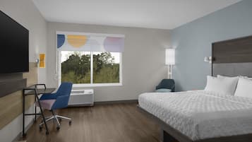 A hotel room with a bed, a desk, a chair, a TV, and a window with blinds.