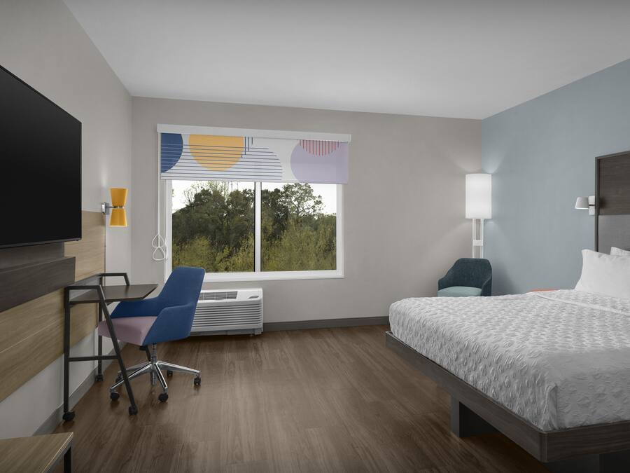 A hotel room with a bed, a desk, a chair, a TV, and a window with blinds.