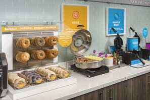 Estación de desayuno con bagels, donas y muffins ingleses.