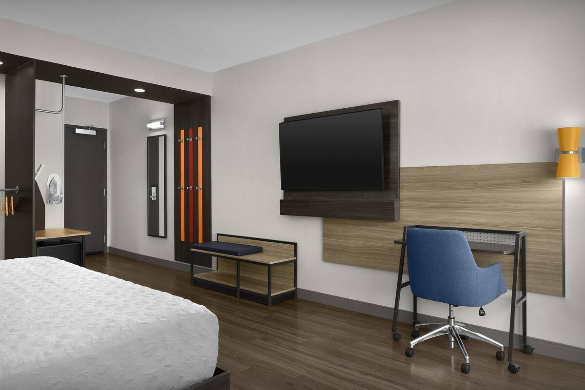 Una habitación de hotel con cama, escritorio, silla, televisor y lámpara.