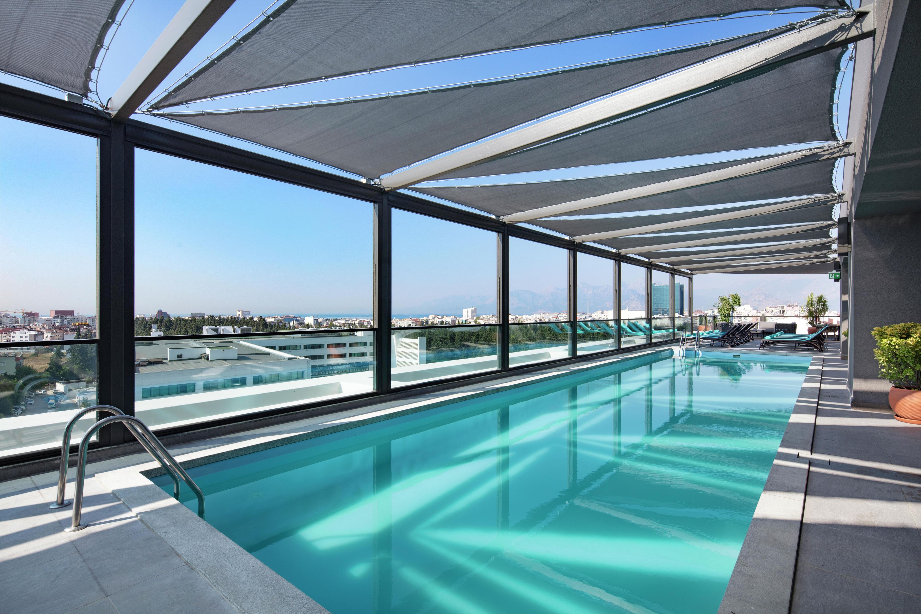 Piscina infinita en la azotea con agua azul cristalina, rodeada de amplias ventanas que ofrecen vistas de la ciudad.