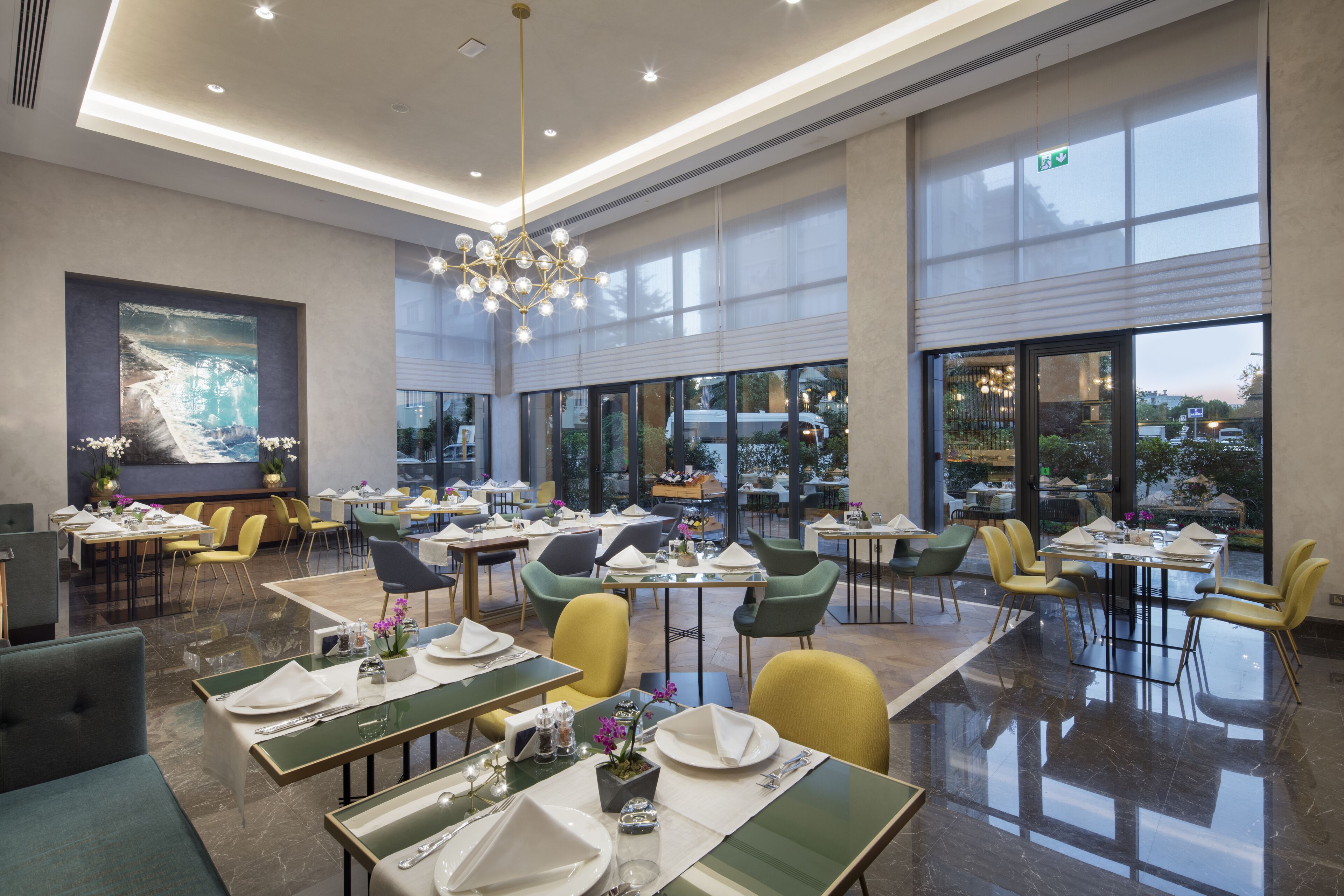 Un comedor espacioso con varias mesas y sillas, ventanas amplias y una lámpara moderna.