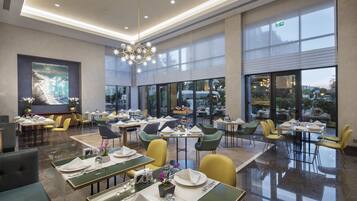 Un comedor espacioso con varias mesas y sillas, ventanas amplias y una lámpara moderna.