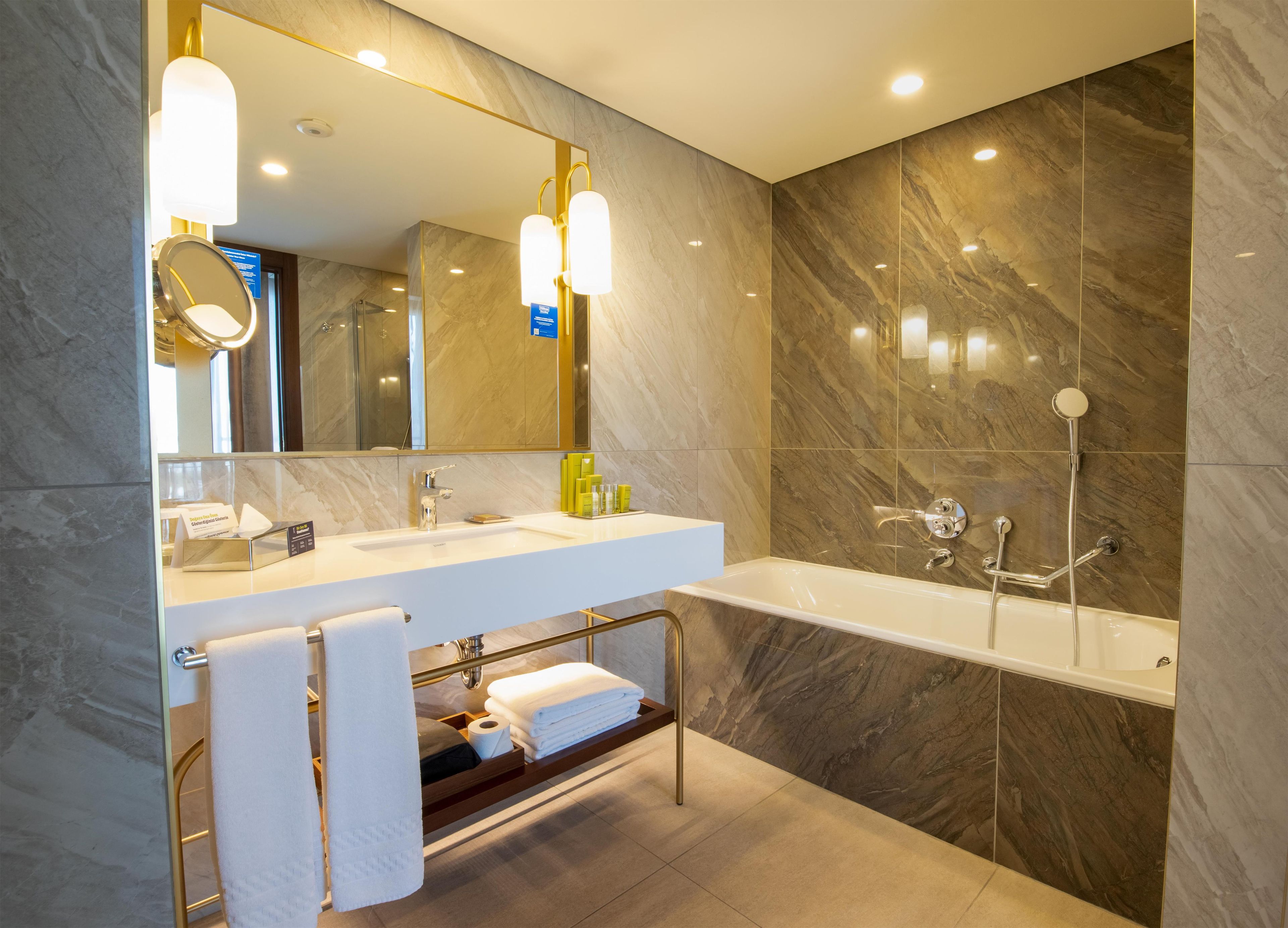 A modern bathroom with a large mirror, a white sink, and a bathtub.