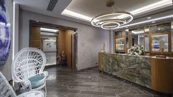 A reception area with a marble counter, a white wicker chair, and a modern chandelier.