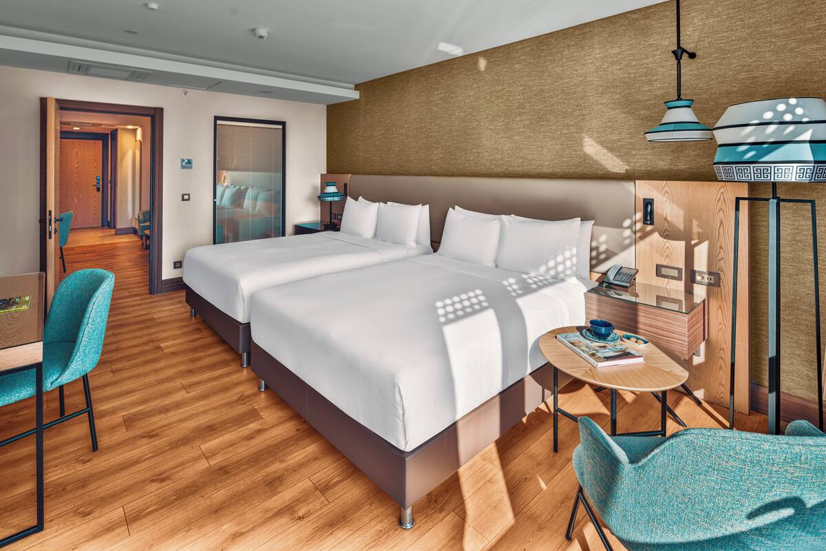 A hotel room with a large bed, a desk, two chairs, and a small table with a lamp.